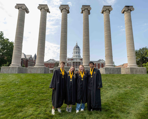 Students in graduation gowns in front of columns.
